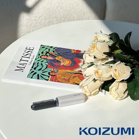 一個白色帶有黑色梳齒的迷你瀏海梳，擺放在一本MATISSE畫冊旁，畫冊上有兩個人物正在彈奏樂器，旁邊還有一束香檳色玫瑰。