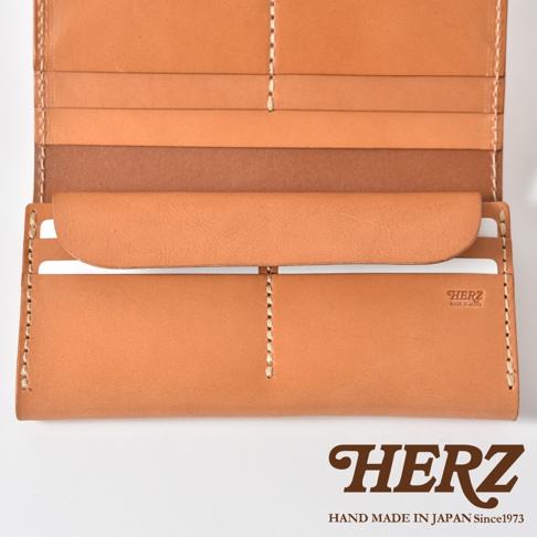 這是一款日本HERZ手工製作的皮革長夾，採用原色植鞣革材質，呈現溫潤的淺棕色調。長夾展開後可見豐富的卡片收納夾層，中央帶有HERZ品牌壓印標誌，整體設計展現粗獷質樸的職人手縫質感與實用性。