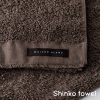 MAISON BLANC 標籤的深棕色柔膚匹馬棉毛巾，毛圈細緻，邊緣有流蘇設計，質感柔軟。