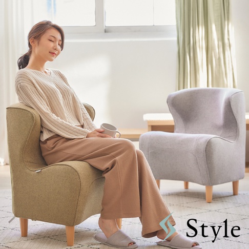 一位女士坐在綠色布藝的「Chair DC 美姿調整座椅」，手中拿著杯子，另一張灰色座椅在後方。