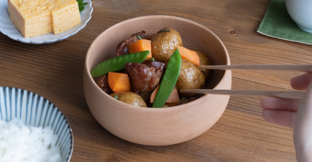 楓木沙拉碗盛有燉煮的馬鈴薯、紅蘿蔔塊、肉塊和毛豆，碗呈淺木色，質地光滑。