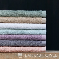 疊放著八條長纖維浴巾，顏色由上至下分別為：薄荷綠、米褐、白色、淺藍綠、薰衣草紫、灰藍、淺粉紅，以及最底部的淡粉色。浴巾材質看起來柔軟蓬鬆，邊緣有精緻的織邊。