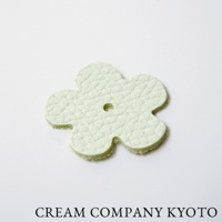 淺綠色皮革製成、五瓣花朵造型的飾品，帶有細緻皮革紋理，中央有一個小圓孔。