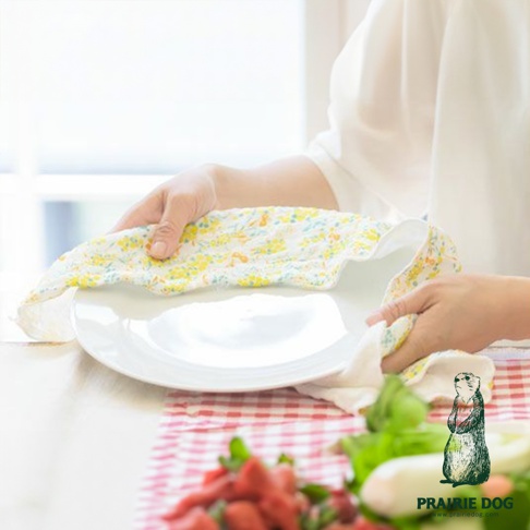 一塊印有黃色小碎花圖案的五層紗質地擦拭巾，正被雙手用於擦拭一個白色的盤子。