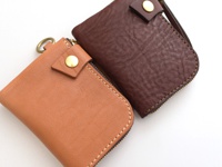 兩款職人手作皮革短夾，一款為棕褐色，另一款為深棕色，皆採用獅鬃風皮革製作，配有黃銅色金屬拉鍊、按扣及掛環。