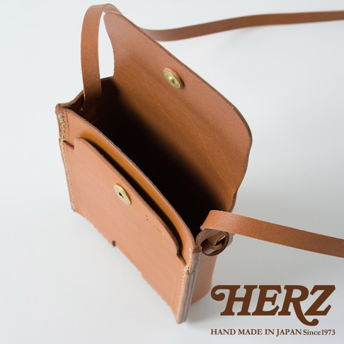 職人手作皮革手機包，淺棕色，翻蓋設計，內部空間和外部口袋，搭配細皮革背帶，附有金屬按扣。