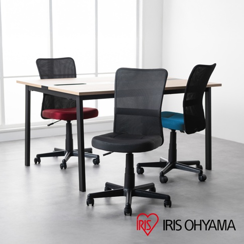 辦公室內一張淺色桌面、黑色金屬桌腳的長方形會議桌，桌旁擺放著四張網狀材質的辦公椅，分別為紅色、黑色、藍色和黑色。