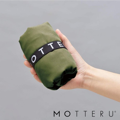 手持一卷綠色摺疊環保袋，袋身以黑色織帶束緊，織帶上有白色英文字母「OTTERU」。