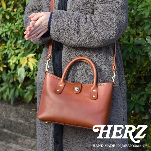 職人手作皮革迷你托特包 T-11，採用鞣製皮革製成，呈現自然棕色調，配有短提把和可拆卸長背帶，包身簡約，綴有金屬釦和鉚釘，適合日常攜帶。