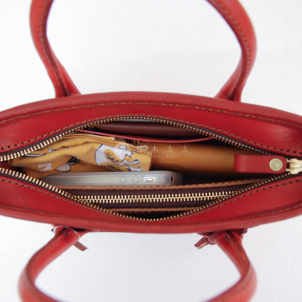 紅色皮革手提包，內部可見手機、黃色印花布料及棕色皮夾。包身採用拉鍊開合，配有提把。