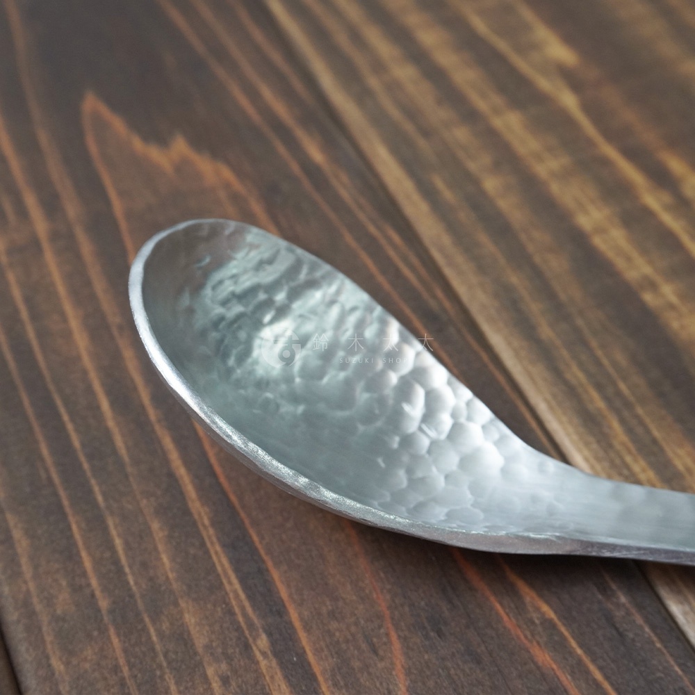 銀色鋁製湯勺，表面有錘目紋，勺身中型，置於深色木紋背景上。