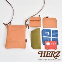 職人手作皮革直式隨身單肩包，搭配同色系皮革零錢包、長夾，以及橄欖綠皮革收納袋、藍色印花手帕與紅色造型卡夾，展現精緻工藝。