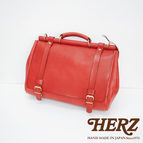 HERZ 職人手作紅色皮革側背包，具有金色扣環和提把，背面有 HAND MADE IN JAPAN Since1973 字樣
