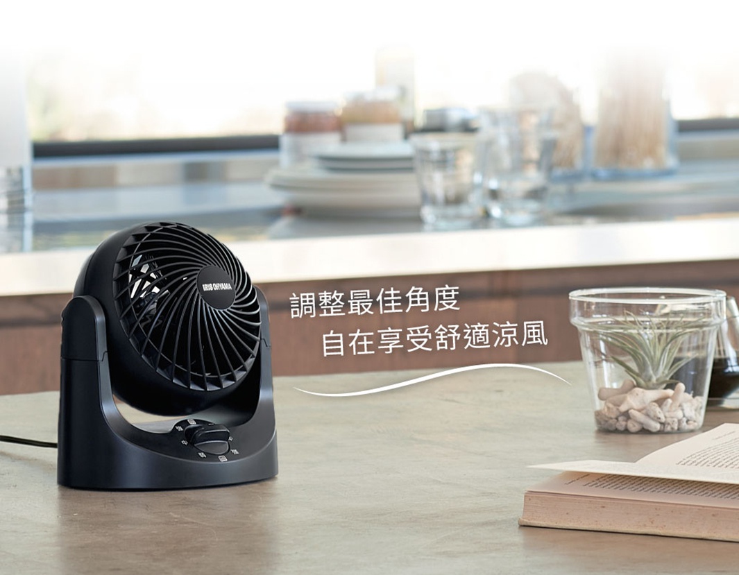 黑色桌上型空氣循環扇，具有可調節的風扇頭和三段風速旋鈕，擺放在木質桌面，旁邊有植物盆栽和書籍。