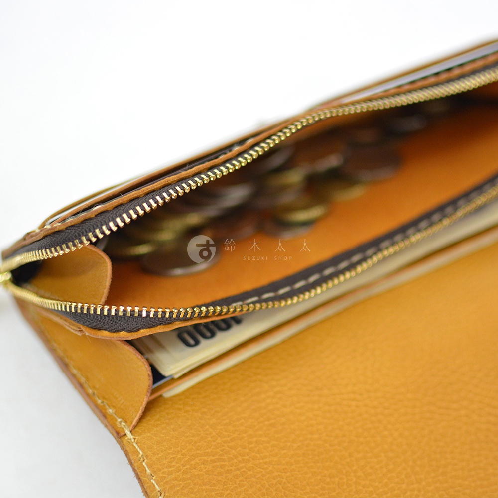 職人手作皮革長夾，顏色為溫暖的芥末黃，展示內部寬敞的收納空間，裝有硬幣及紙鈔，拉鍊為金色，皮革表面紋理清晰。