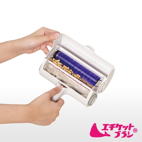 雙層除塵滾輪，白色外殼，內含紫色毛刷滾輪及收集髒污的隔層，裝有貓砂顆粒和棉絮。