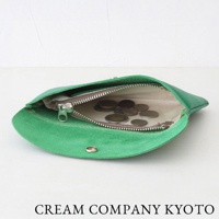 一隻綠色麂皮製成的多功能收納包，拉鍊部分可見內部裝有零錢。收納包以開放式方式展示，底部有金屬按扣。