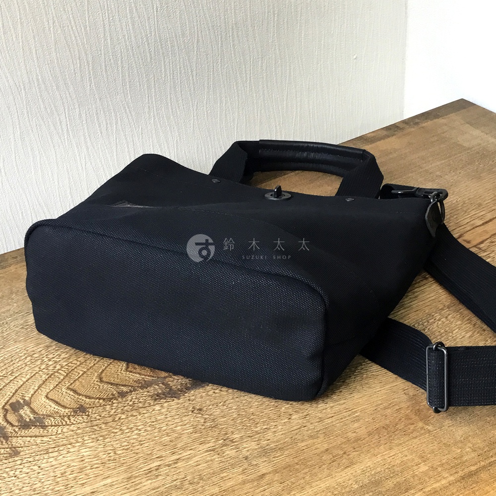 黑色帆布兩用托特包，設有皮革提把和可調節的帆布肩帶。包身呈現方形輪廓，材質可見細緻紋理。