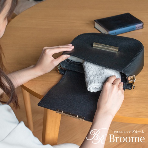 Broome ASH 今治柔韻波紋甘撚手帕，展示一個女人正在將一條灰色的波紋手帕放入一個黑色的皮革包中。