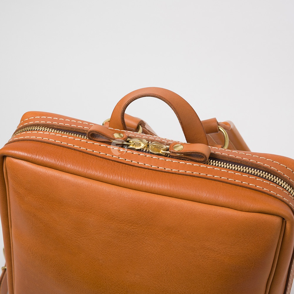 棕色皮革商務後背包，配有金色拉鍊和白色縫線，頂部有一個手提把。