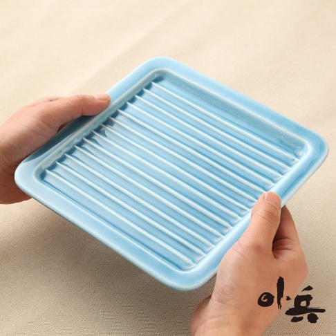 淺藍色美濃燒油切方盤，表面有規律的條紋設計，盤緣略高，由雙手持握展示。