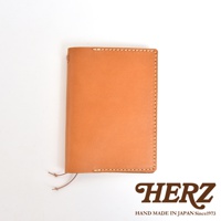 淺棕色皮革手帳套，縫線清晰，右下角有HERZ品牌標誌和HAND MADE IN JAPAN Since1973字樣
