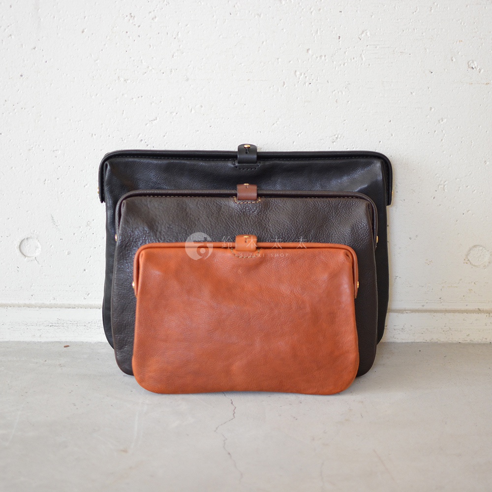 職人手作皮革Organ手拿包，展示黑色、深棕色和橘棕色三款，皆為皮革材質，具有金屬開合扣，呈現不同尺寸的堆疊擺放。