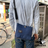 深藍色刺子織迷你側背包，斜挎於身穿條紋襯衫的模特身上，包身有菱格紋縫線和品牌標籤，搭配黑色可調式背帶。