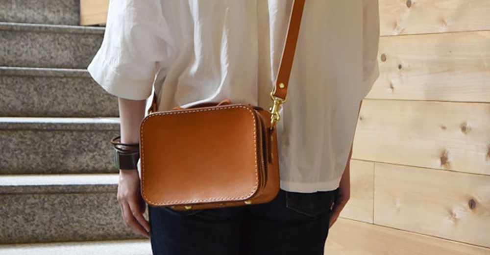 日本HERZ職人手作皮革兩用迷你小方包，棕色硬皮革材質，可肩背或斜背，配有金色拉鍊與五金。