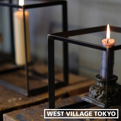 兩個鐵製長方展示架，其中一個架上放置著一支燃燒中的淡粉色蠟燭，另一架內有支米白色蠟燭，背景模糊。
