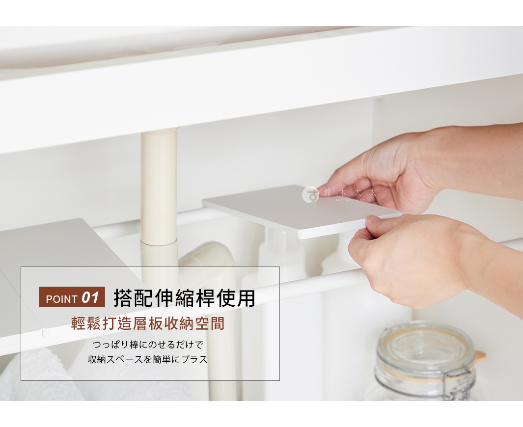 一隻手正將白色塑膠置物板放置在兩根平行伸縮桿上，以此在水槽下方創造出額外的收納空間。置物板呈現簡約的霧面白色，與環境中的水管及收納瓶罐形成對比，展現出利用伸縮桿輕鬆打造層架的居家收納設計。