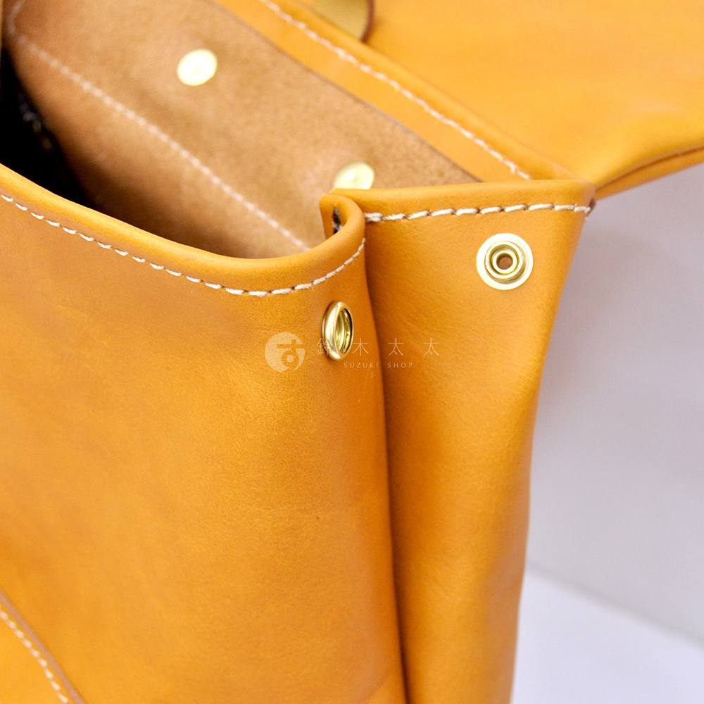 職人手作皮革多口袋後背包 R-135，特寫展示了溫暖的黃褐色皮革材質，細膩的縫線和黃銅色金屬鉚釘細節，展現其精緻工藝。