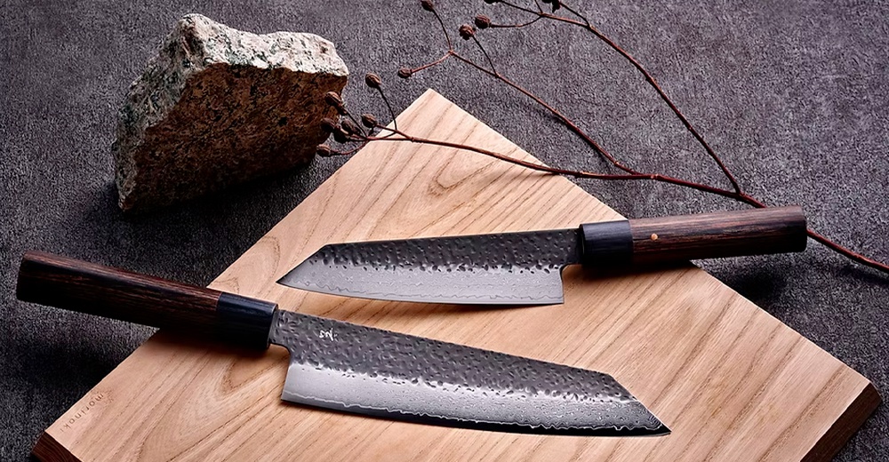 兩把附有黑色木柄的日本廚刀，刀刃呈現錘紋和緞面處理，刀身銀色，刀柄深棕色，擺放在木質砧板上。