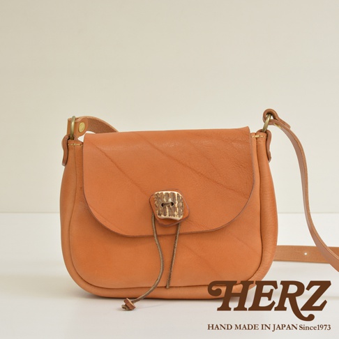 棕色皮革製成的圓形翻蓋肩背包，配有鹿角狀的鈕扣和細繩，風格簡約，適合日常攜帶。