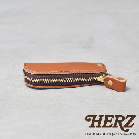 職人手作皮革Organ拉鍊鑰匙包，展示了焦糖色皮革，配有黃銅拉鍊和鉚釘，整體呈圓潤的長方形。