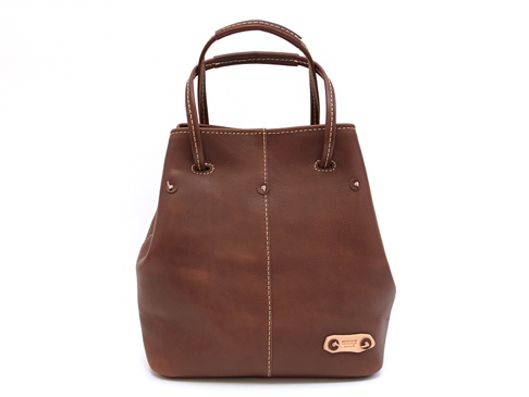 棕色皮革托特包，帶有米白色縫線細節，頂部有兩個手提把，側面有金屬铆釘裝飾，底部有一個品牌金屬銘牌。