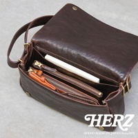 深棕色皮革斜背包，翻蓋設計，內部可見拉鍊夾層、文件和零錢包，材質為Genuine Leather。