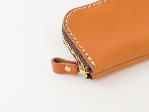 淺棕色皮革迷你錢包，帶有拉鍊和皮革拉頭，以及白色的縫線。