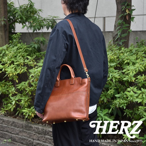 職人手作棕色皮革大容量兩用托特包，附有可拆卸肩帶，包款底部有四個金屬腳釘，整體呈現復古風格。