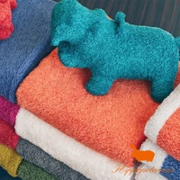 藍綠色竹棉混紡河馬造型抓握玩偶，疊放在橙色、白色、藍色、紅色、綠色等多色毛巾上方。