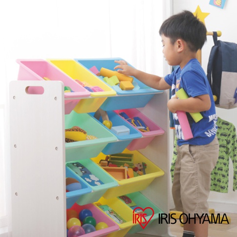 色彩繽紛的童心玩具繪本收納架，共四層，每層有三個不同顏色的收納盒，包含粉色、黃色、淺藍色和淺綠色。收納架本體為白色，由木質材料製成，側邊有提把。架上擺放著各種玩具和繪本，一名男孩正在拿取玩具。