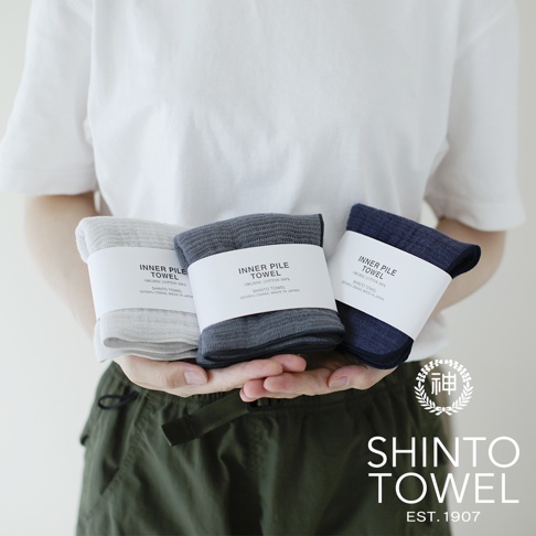 三條 INNER PILE 雙面紗布輕質浴巾，分別為淺灰色、炭灰色與海軍藍，均以白色標籤包裝，標籤上印有產品名稱與製造資訊。