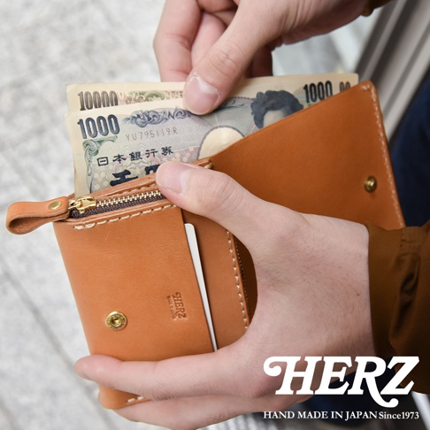 職人手作皮革小型雙折短夾，棕色皮革，內有日圓鈔票，拉鍊細節清晰可見。