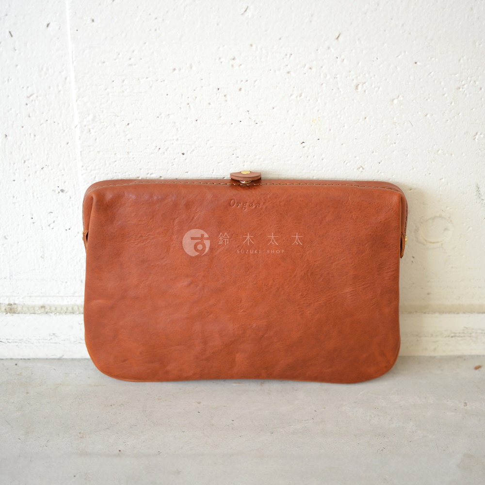 職人手作皮革Organ手拿包，焦糖棕色，光澤溫潤，質感柔軟。包款簡潔，配有金屬按扣開合，適合日常攜帶。