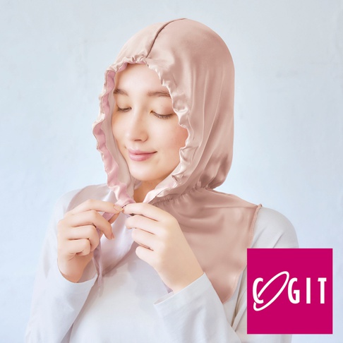 淺粉色絲質柔順的睡帽，帶有荷葉邊裝飾，由一位女性佩戴，她正用雙手調整睡帽。