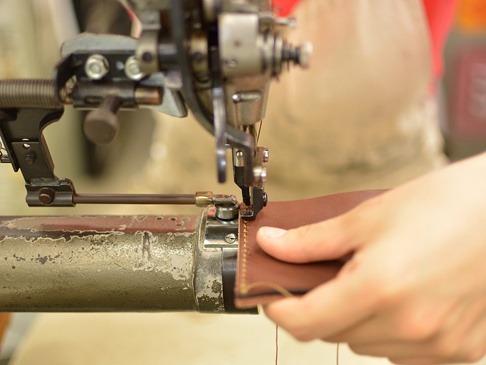 職人手作皮革存摺文件收納夾，棕色皮革，正在使用工業縫紉機進行縫製，展示製作過程。