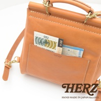 職人手作皮革屋瓦風後背包，淺棕色皮革，包身縫線明顯，正面有一個較大的置物袋，內有雜誌和地圖。