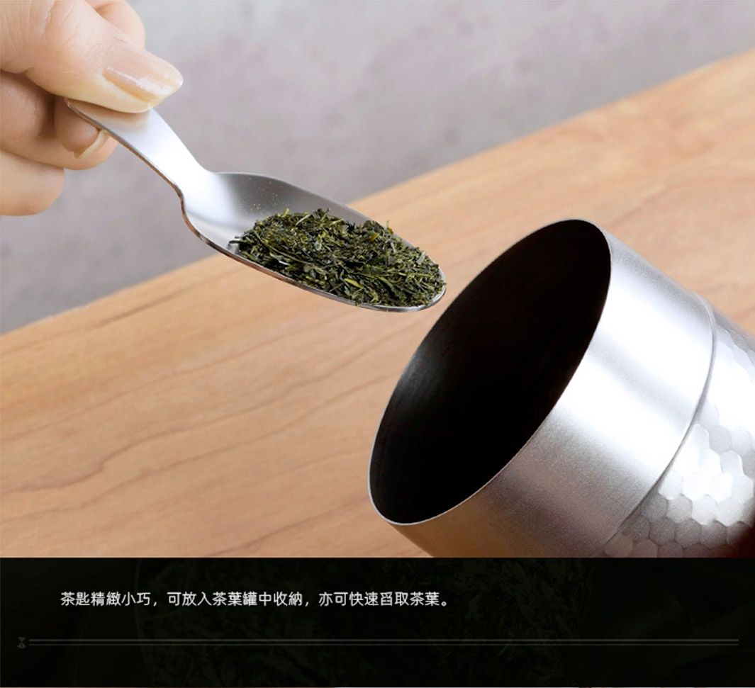 日製18-8不鏽鋼錘目紋茶葉罐，附有同材質的茶匙，茶匙中盛有細碎的綠色茶葉，茶葉罐為銀色，表面有錘擊紋理。