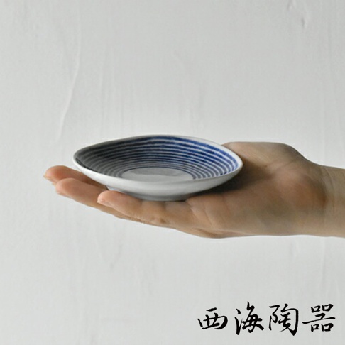 一隻手掌托著一個波佐見燒藍玉紋五件式醬料碟。碟子為白色陶瓷，內側飾有藍色同心圓紋路，邊緣略有起伏。