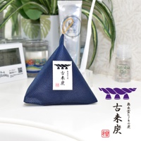 深藍色網狀材質的立體三角調濕木炭，頂部有金色繩圈，正面貼有白色標籤，上面有日文文字和一個黑色圖案。